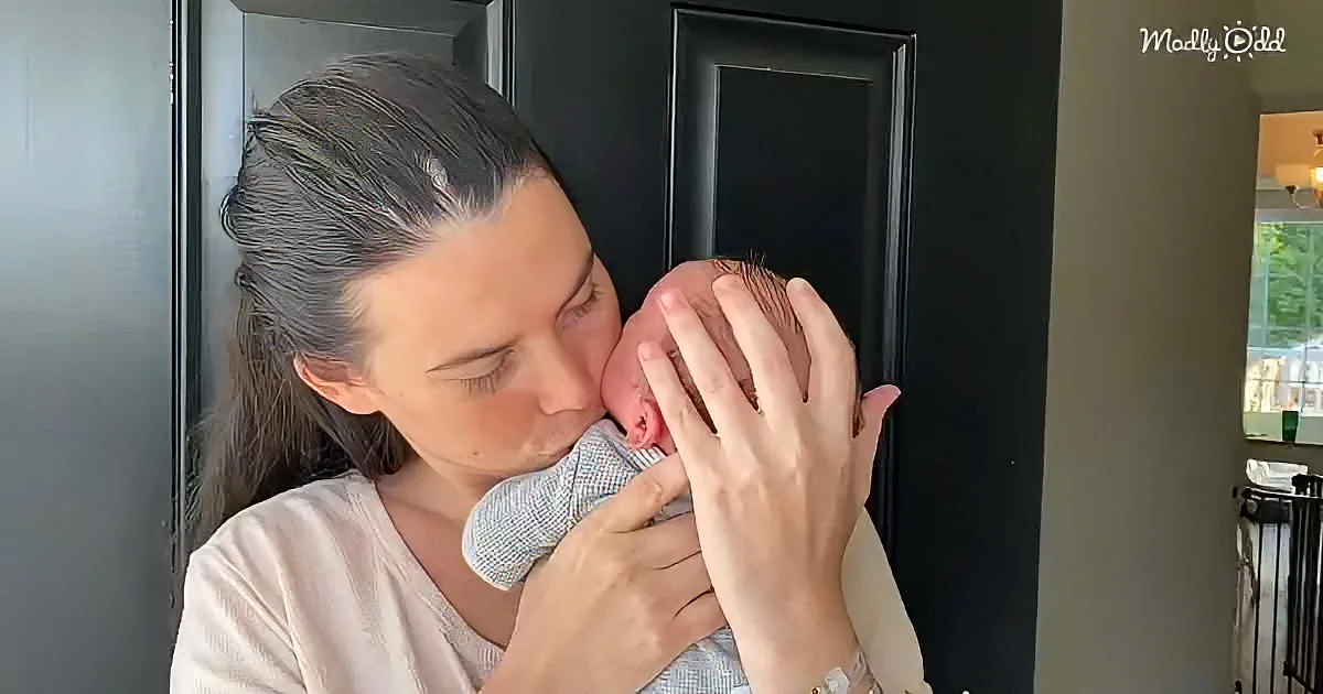 A woman holds and gently kisses a newborn baby wrapped in a blue blanket.