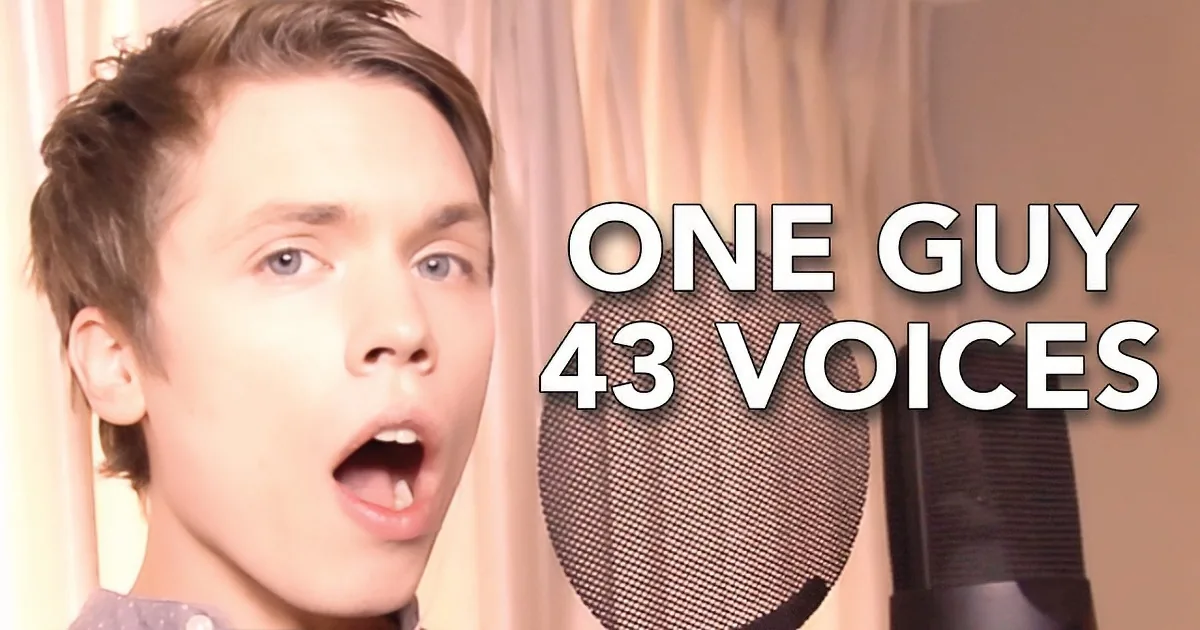 A person in a grey hoodie speaks into a microphone, with a blurred background showing a room and a piano.