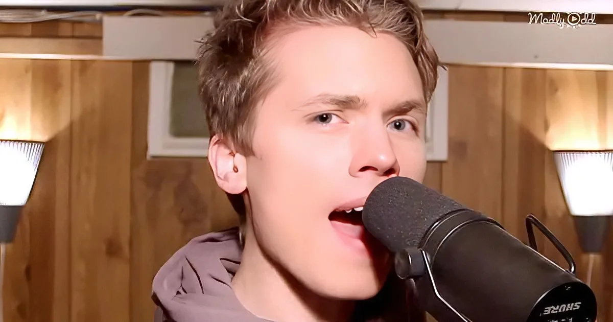 A person sings into a microphone in a room with wooden walls and a light fixture.