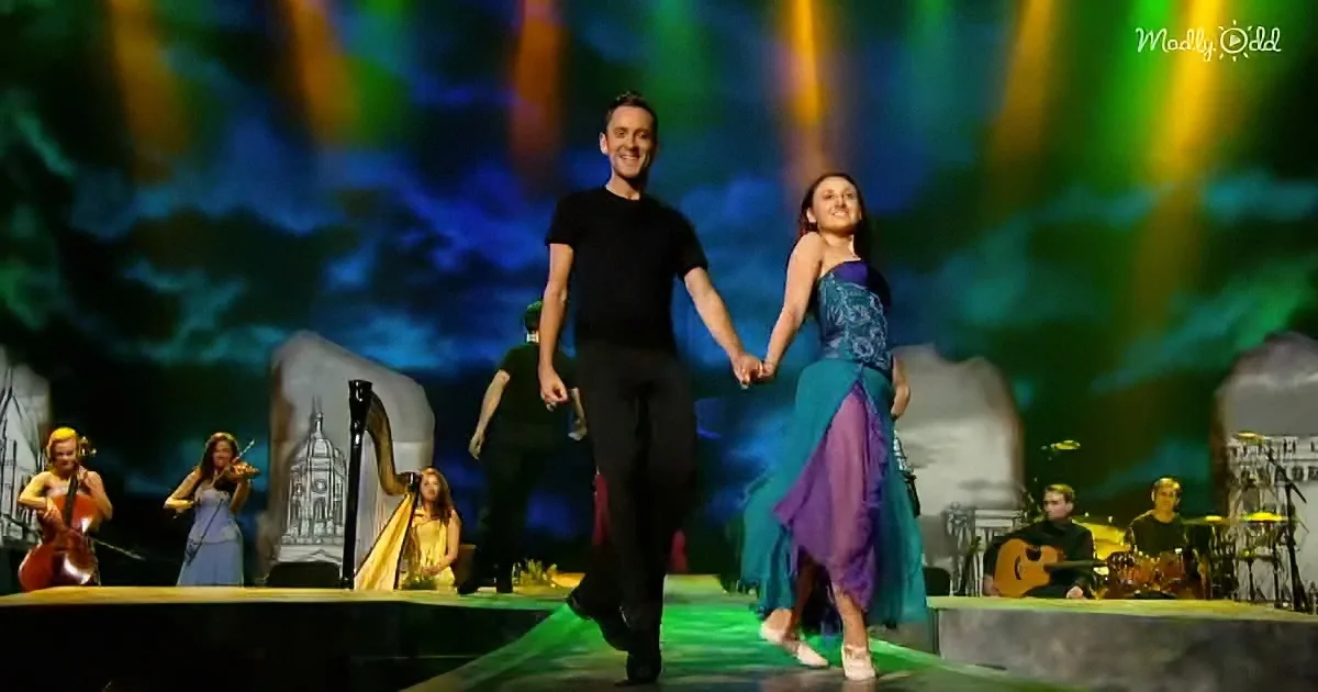 A couple holds hands on stage, surrounded by musicians and a colorful backdrop.
