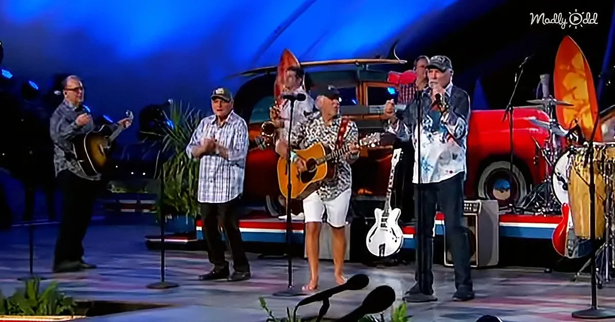 A group of musicians perform on stage with guitars and microphones, surrounded by vintage cars and surfboards.