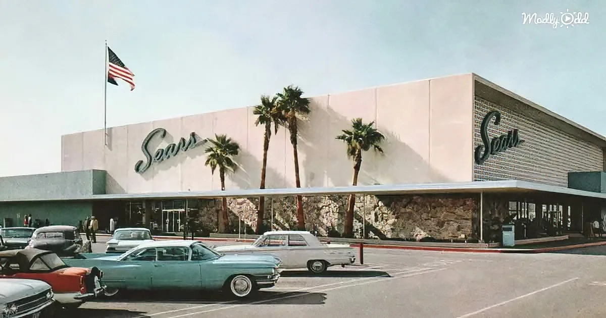 A vintage Sears store with palm trees, classic cars, and an American flag in front.