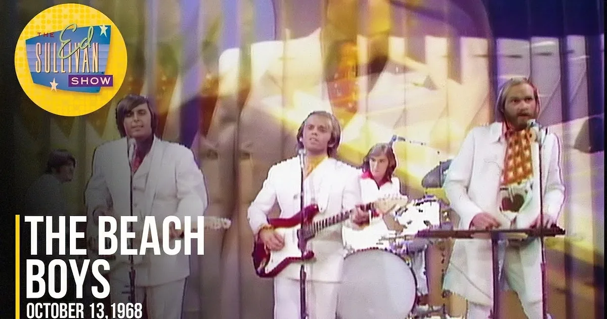 A band in white suits performs on stage with a large yellow background.