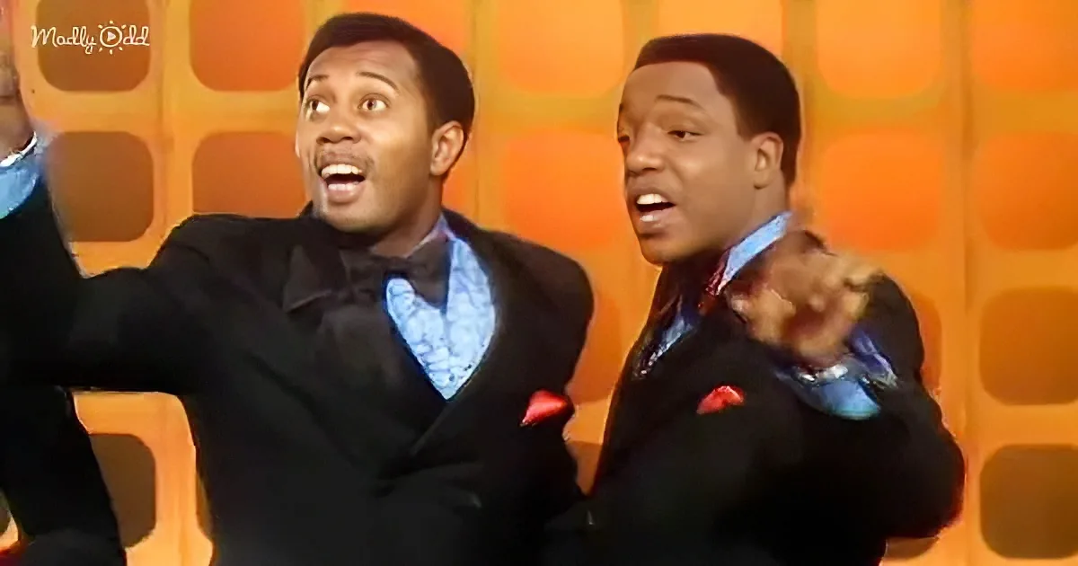 Two men in suits with vibrant blue and red accents, performing energetically on stage.
