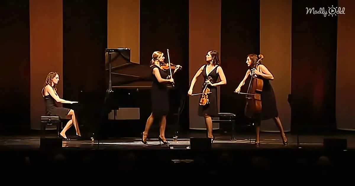 Four women play classical instruments on stage, with a grand piano in the background.