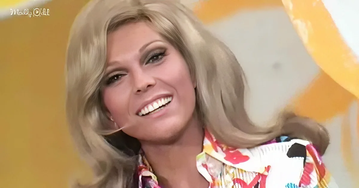 A smiling woman with blonde hair, wearing a colorful patterned shirt, against a yellow background.