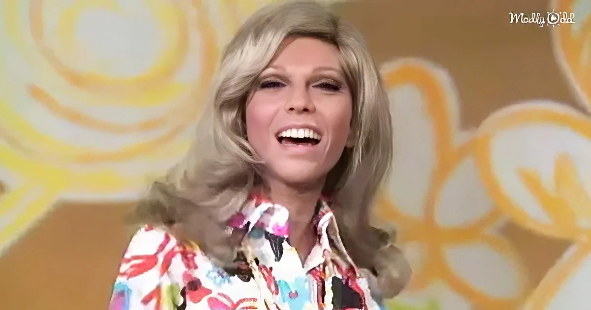 A woman with long, wavy blonde hair smiles widely, wearing a colorful floral shirt against a yellow and white patterned...