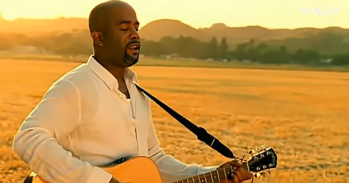 A man in a white shirt plays an acoustic guitar in a field at sunset.