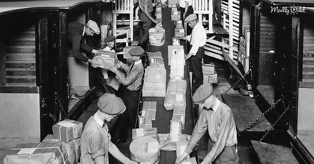 Men in hats load packages into a train car, surrounded by boxes and crates.