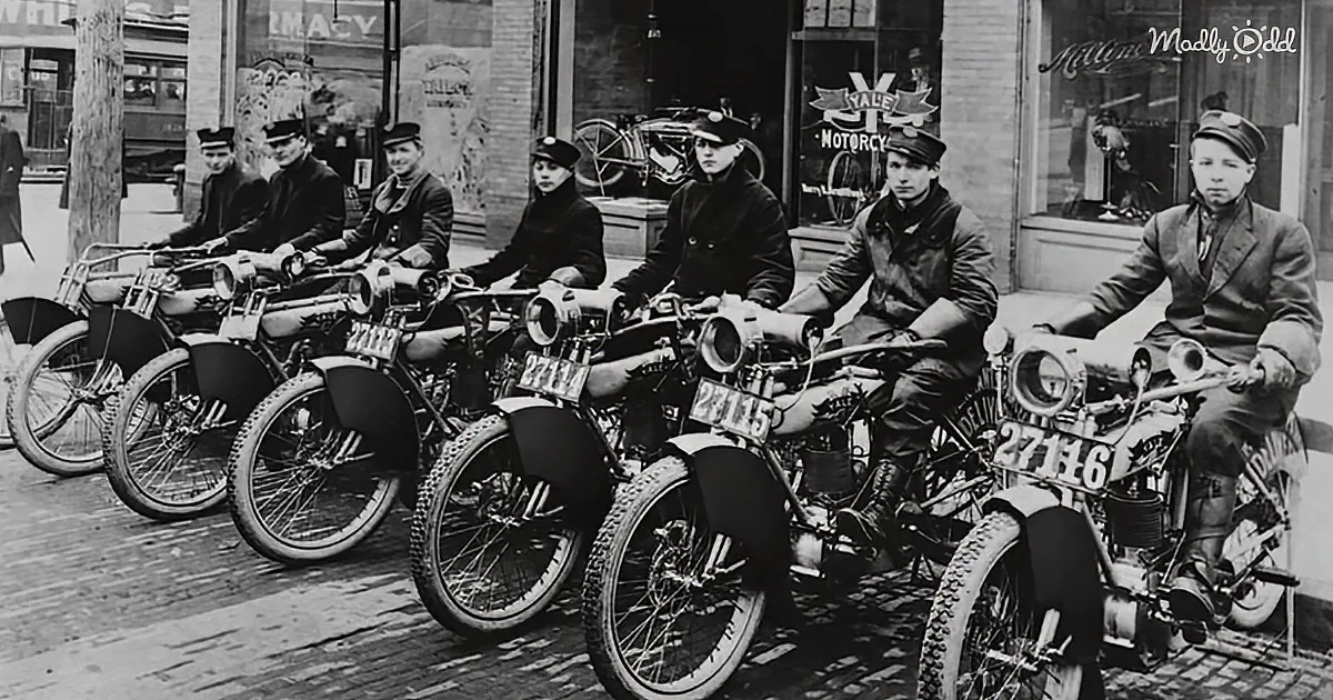 Six uniformed men sit on vintage motorcycles in a row, parked on a cobblestone street.