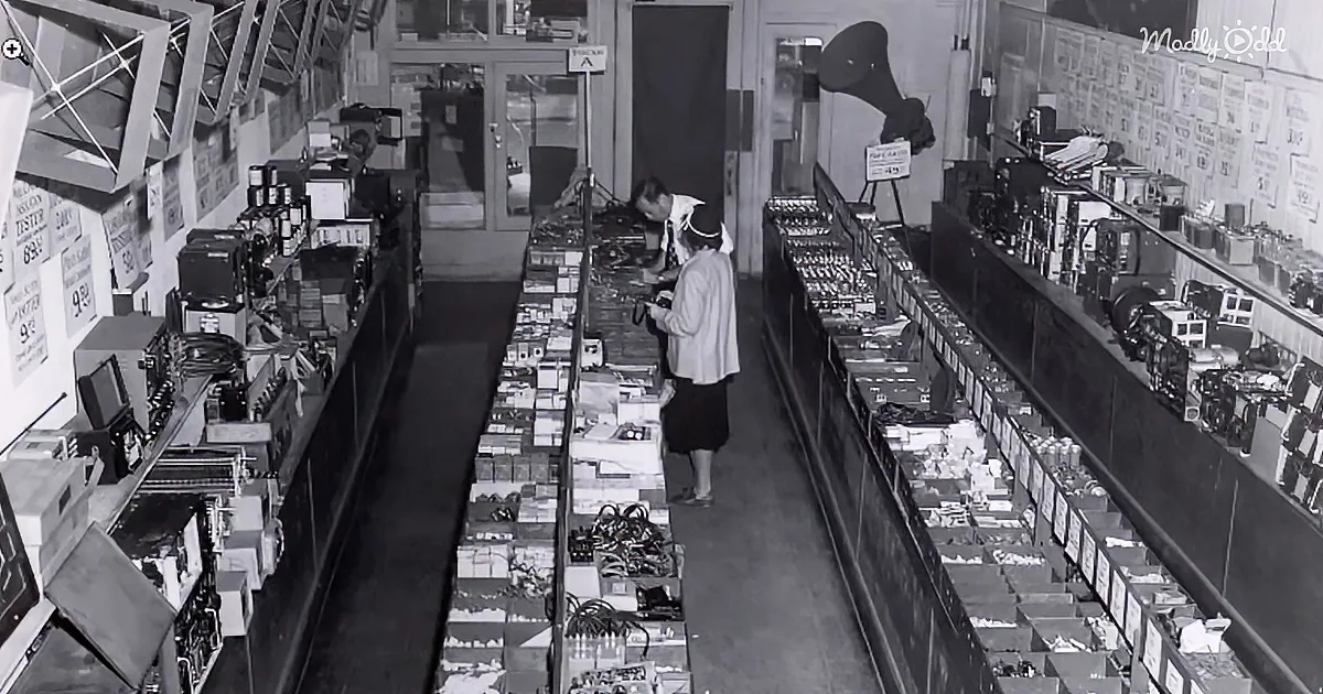 A woman browses electronics in a vintage store with neatly arranged shelves and signage.