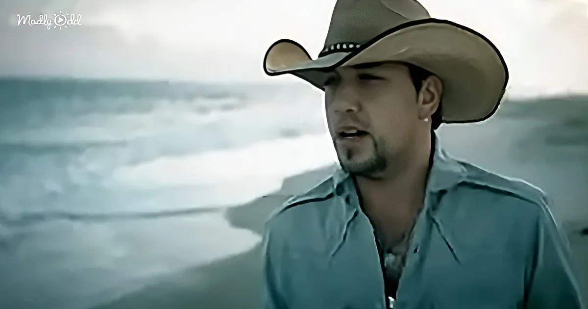A man in a cowboy hat and teal shirt stands by the ocean, looking contemplative.