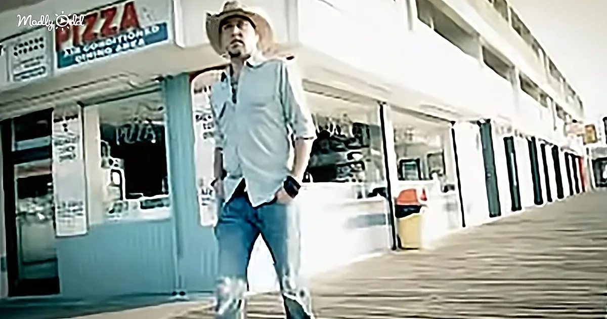 A man in a hat and jeans walks past a pizza shop with a blurred background.