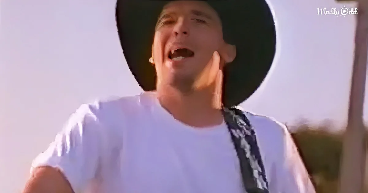 A man in a white shirt and black hat is singing outdoors, with a blurred background.