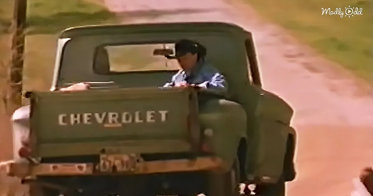 A person sits in the back of a green Chevrolet truck on a dirt road.