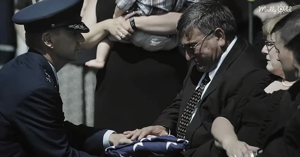 A man in uniform hands a folded flag to another man in a suit at a solemn ceremony.
