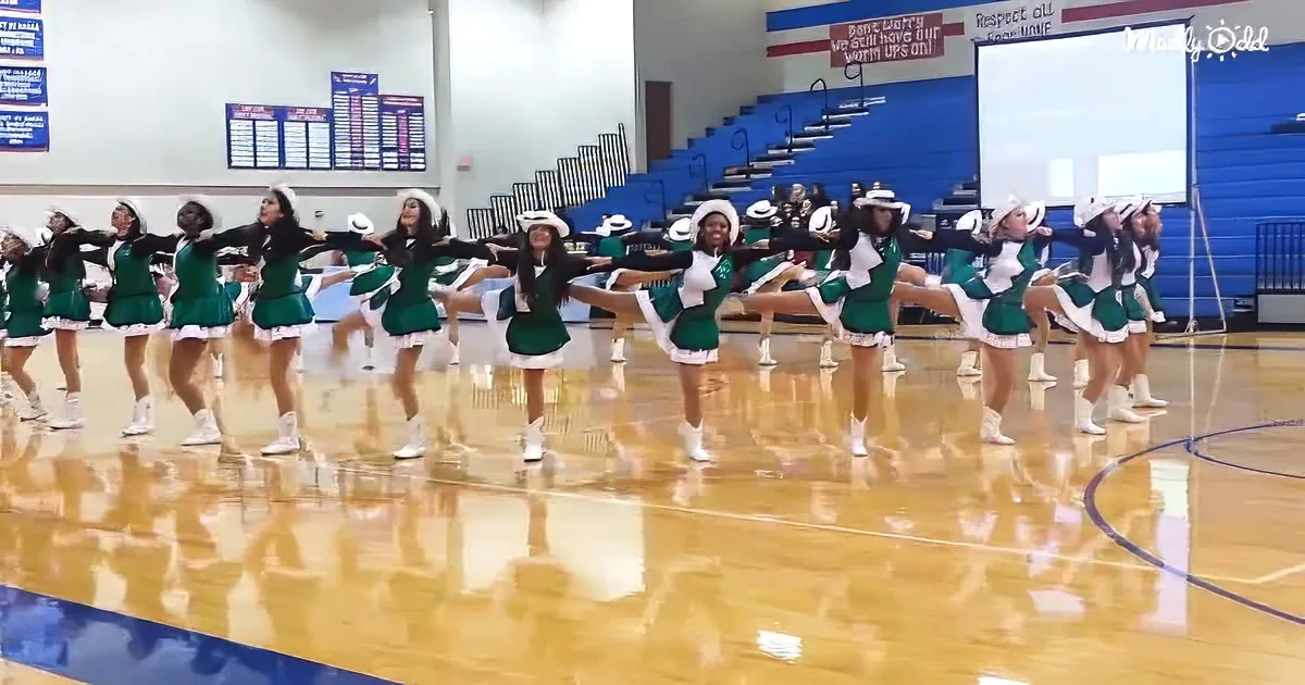 Cheerleaders in green uniforms perform a synchronized routine on a gymnasium floor.