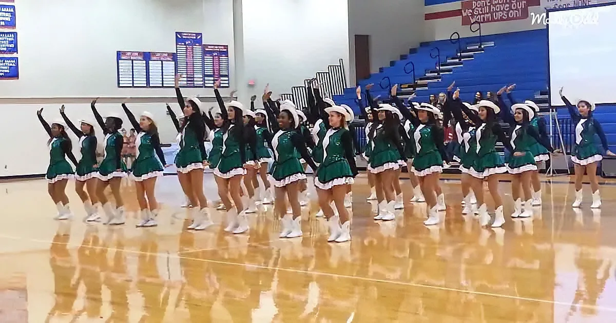 A group of cheerleaders in green uniforms perform a routine on a gymnasium floor.