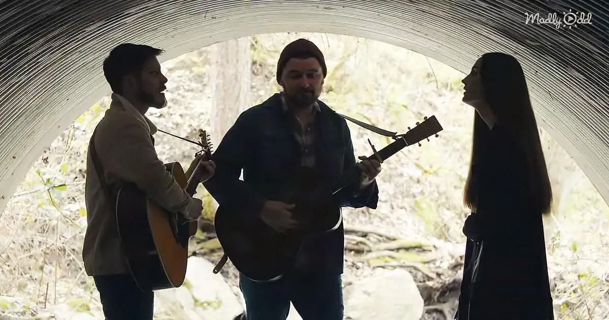 Three musicians play guitars inside a tunnel, with a woman standing nearby.