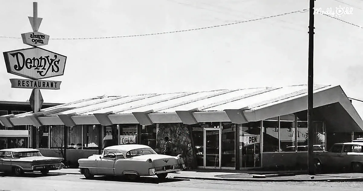 Denny's restaurant sign and building with cars parked in front, vintage style.