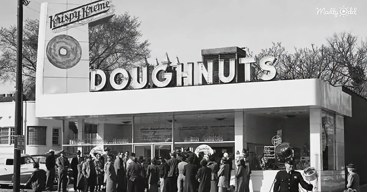 A crowd gathers outside a Krispy Kreme doughnut shop with a large sign and a donut illustration.