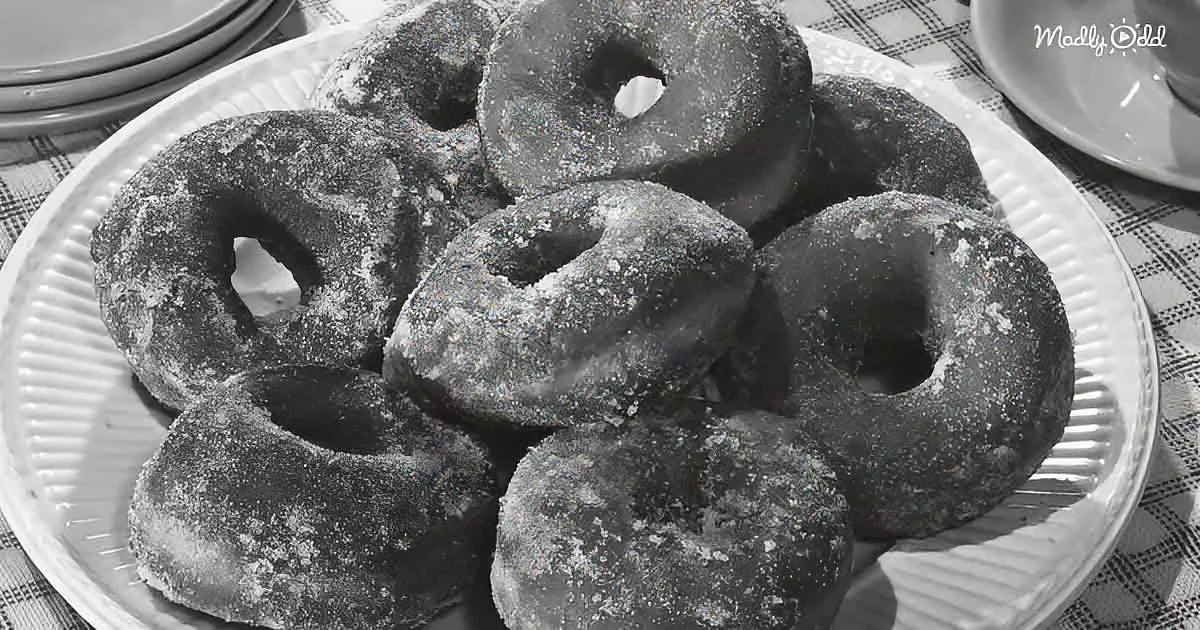 A plate of powdered sugar-coated donuts sits on a checkered tablecloth.