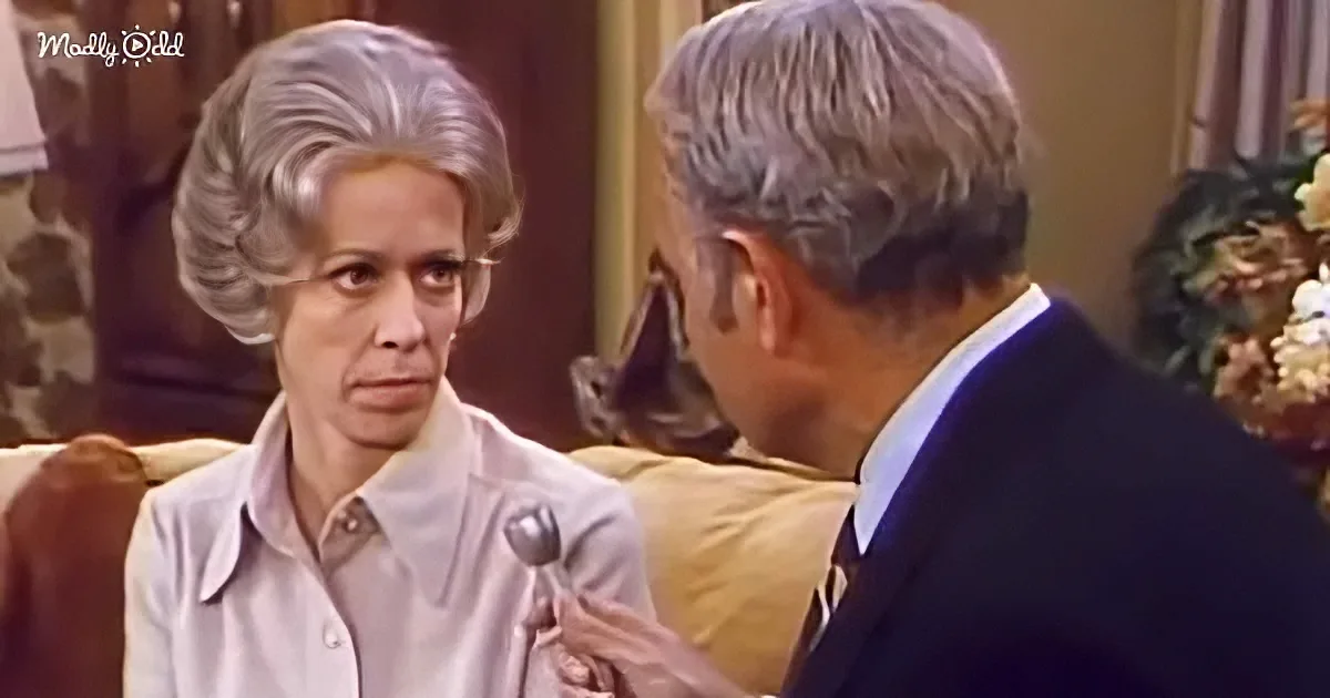 A woman with a concerned expression sits on a couch, facing a man in a suit who holds a spoon.