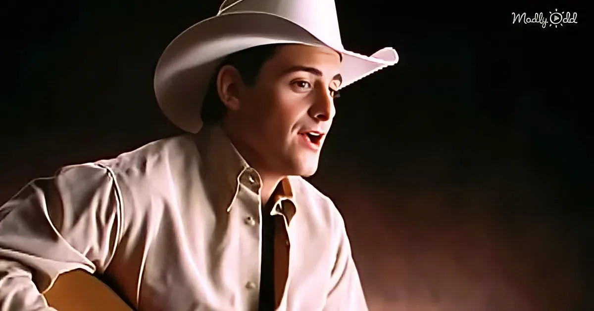 A man in a white cowboy hat and shirt sings while holding a guitar.