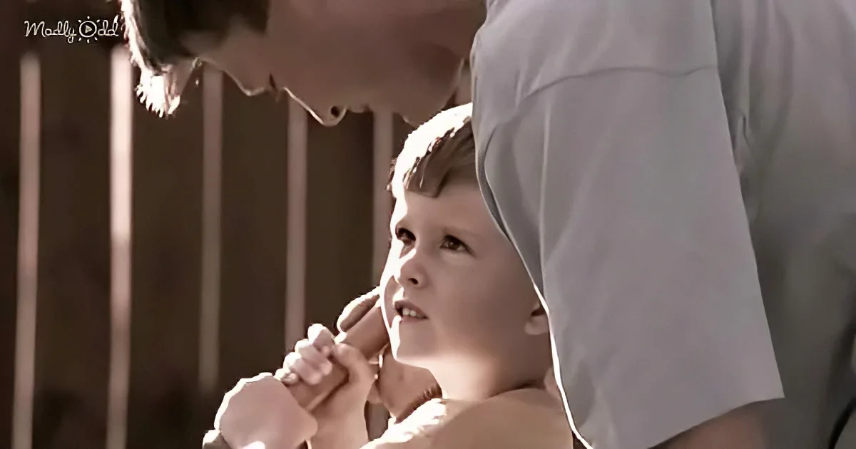 A young boy holding a microphone, looking up at a person leaning over him.
