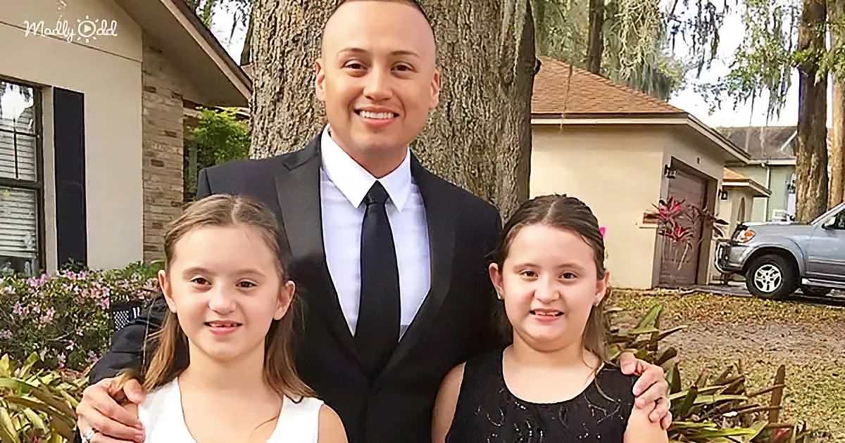 A man in a suit stands with two young girls in a suburban setting, smiling.