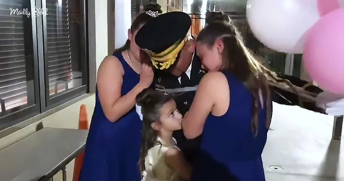 A woman in a blue dress is hugging another woman in a police uniform, with a young girl in a white dress looking on.