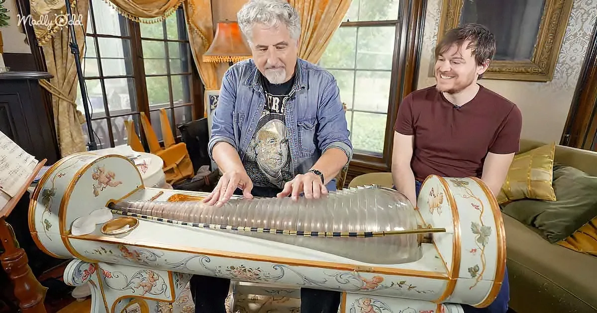 Two men examine a large, ornate, transparent instrument with decorative patterns.
