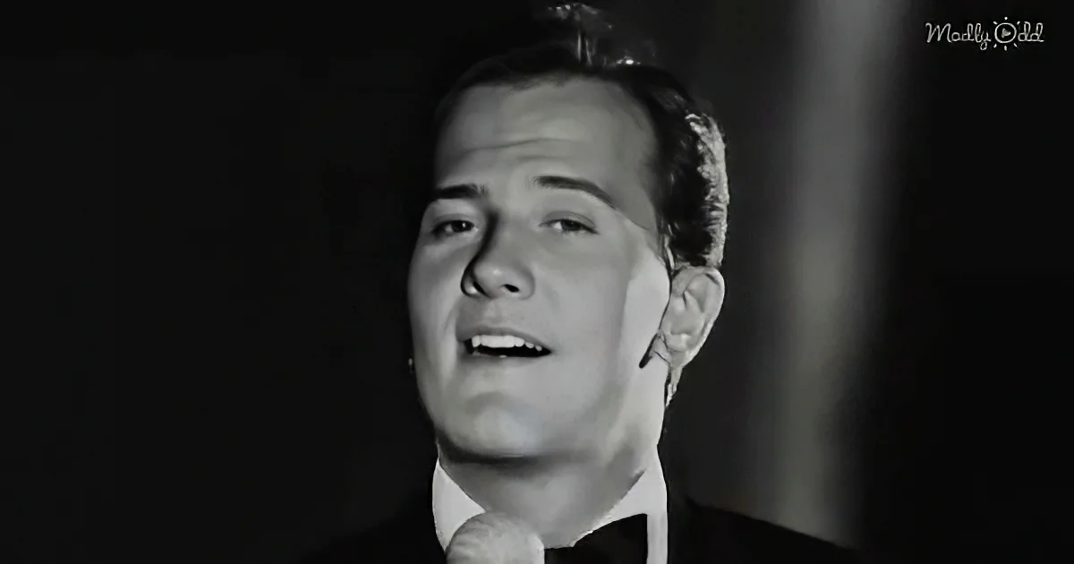 A man in a suit sings into a microphone, his mouth open, in a black-and-white image.