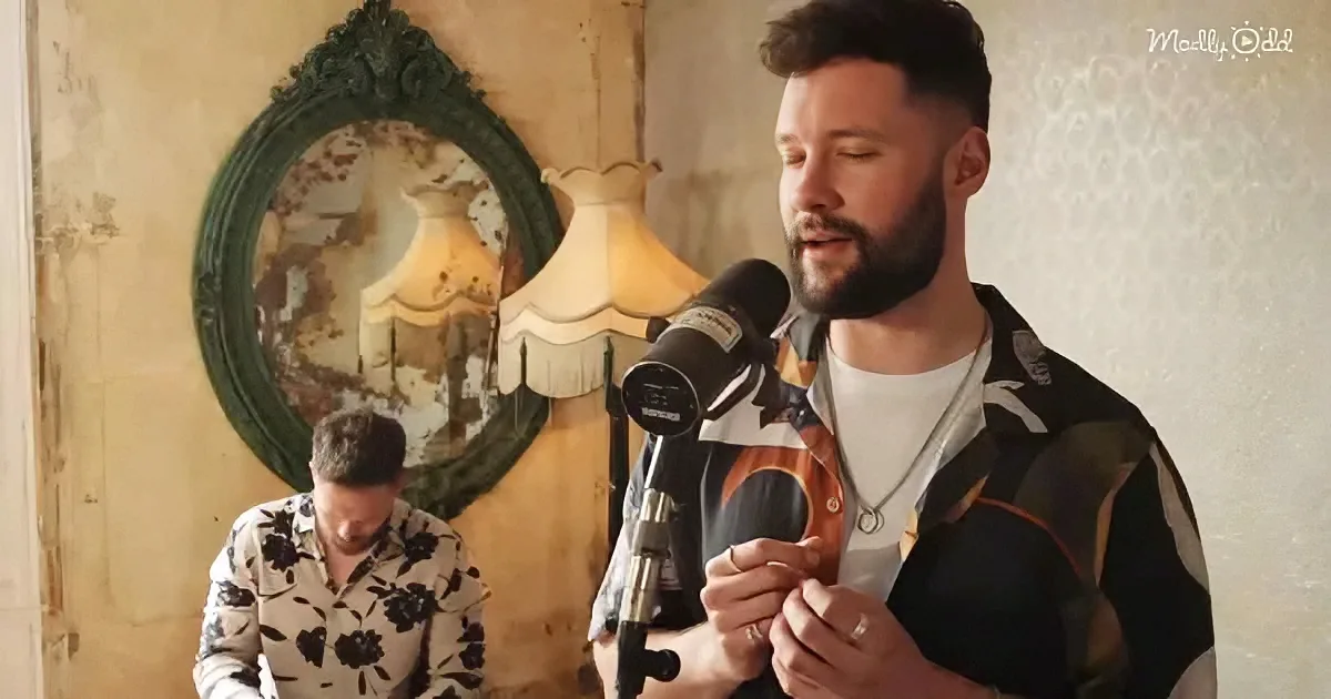 A man with a beard sings into a microphone, wearing a patterned shirt, with another person in floral attire in the...