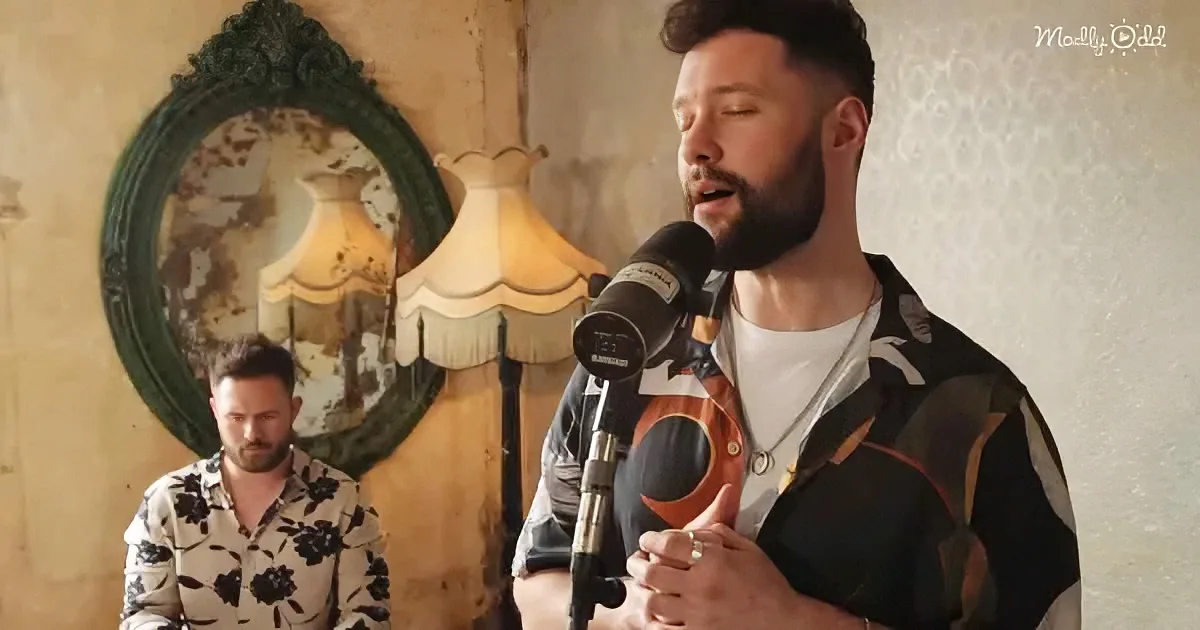 A man with a beard sings into a microphone, wearing a patterned shirt, with another man in a floral shirt standing behind...