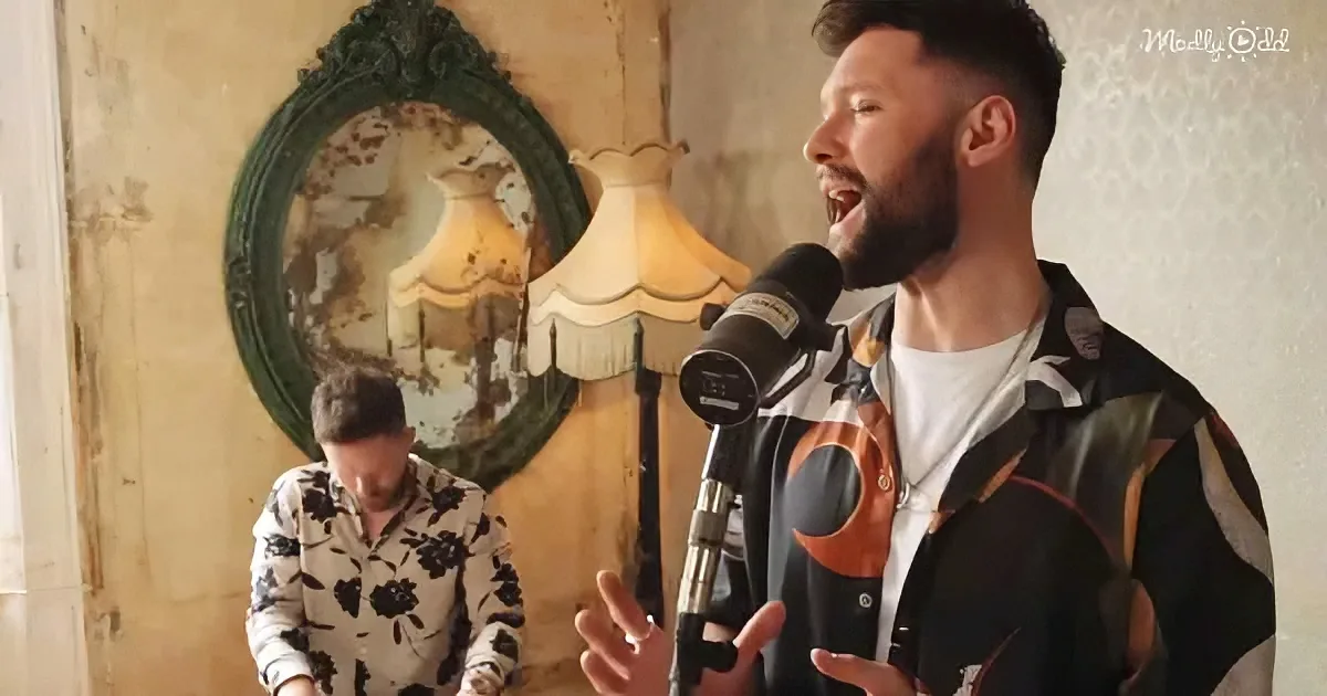 A man in a patterned jacket sings into a microphone, gesturing with his hands, with another man in a floral suit seated...