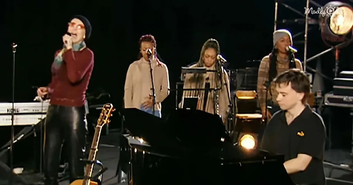 A woman in a maroon sweater sings into a microphone on stage with a band.