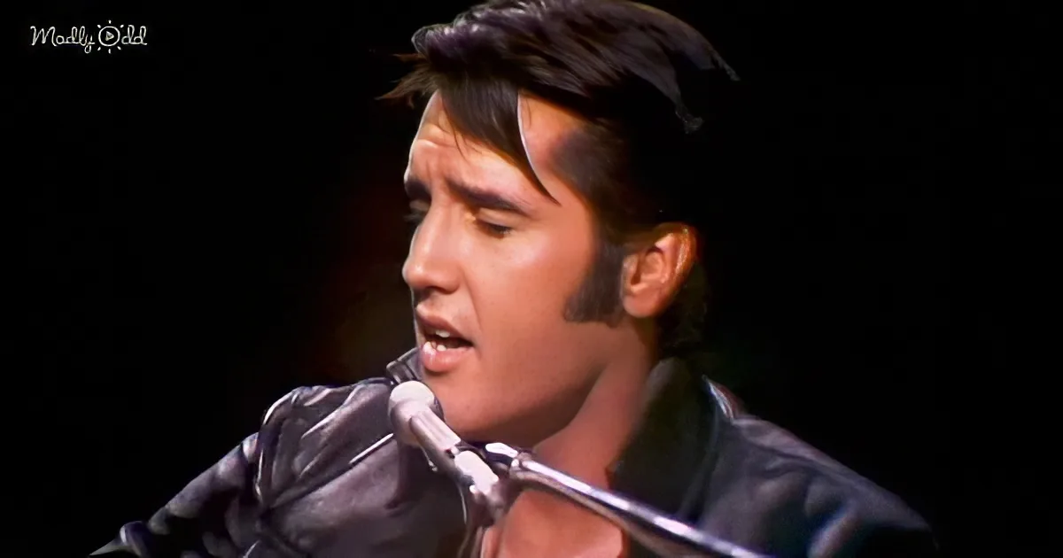 Elvis Presley singing into a microphone, wearing a black leather outfit, with a dark background.