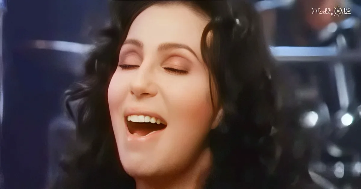 A woman with dark hair and closed eyes is singing, wearing headphones, with a blurred background.