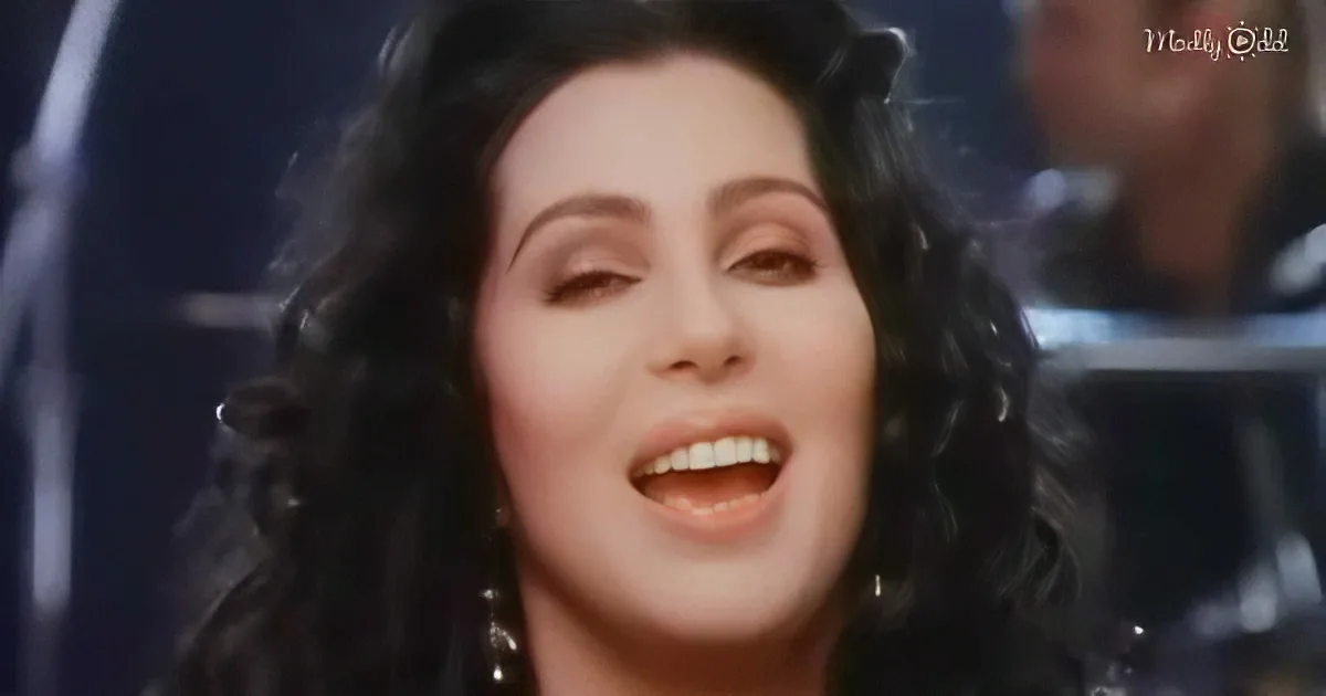 A woman with long dark hair and earrings is singing with her eyes closed, mouth open.