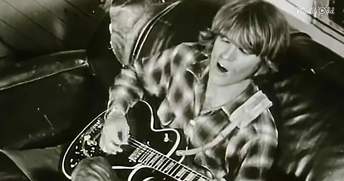A person in a plaid shirt plays a guitar, singing passionately.