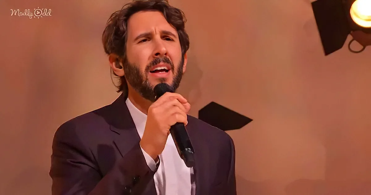 A man with curly hair and a beard sings into a microphone, wearing a dark suit and white shirt.