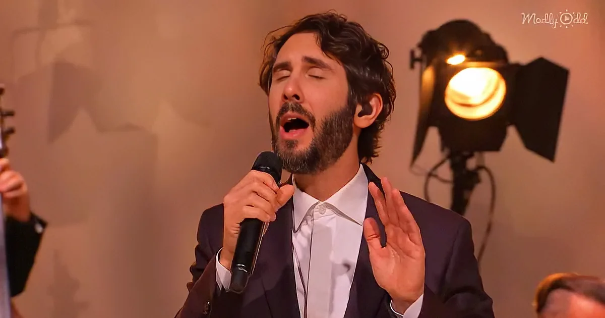 A man in a suit sings passionately into a microphone, gesturing with his hands.