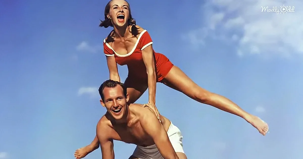 A woman in a red swimsuit is balancing on a man's back, both smiling under a clear blue sky.