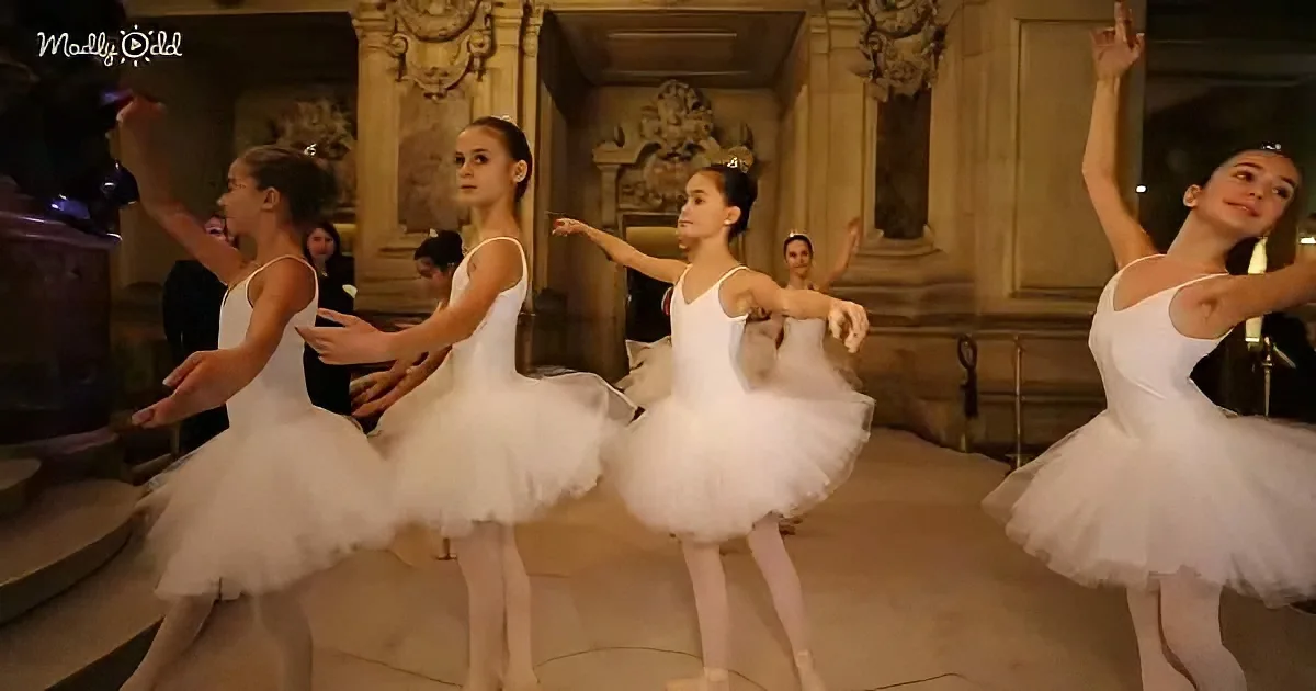 Five ballerinas in white tutus perform gracefully in a grand, ornate setting.