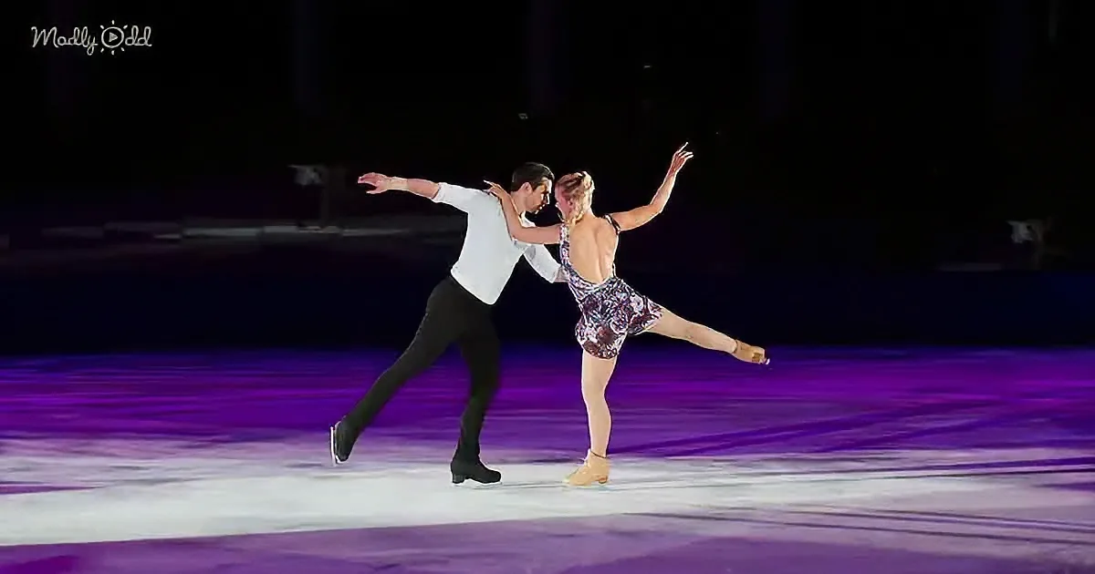A couple in a graceful skating pose on a purple-lit ice rink.