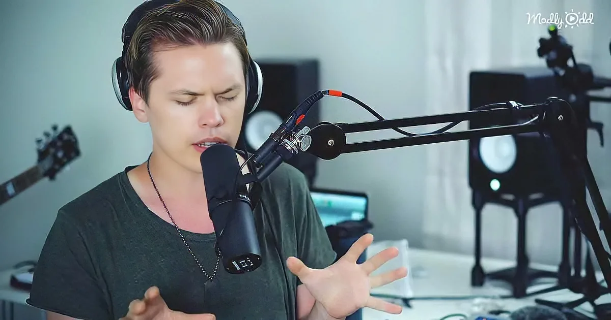 A person wearing headphones sings into a microphone, gesturing with their hands in a recording setup.