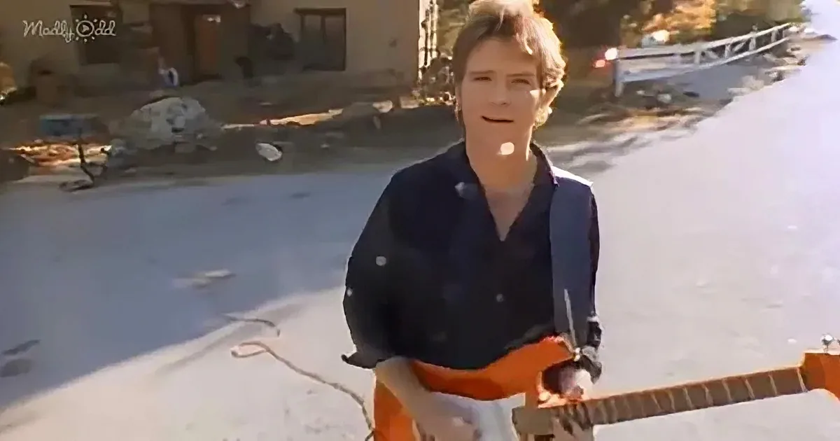 A person in a dark shirt and orange pants stands on a snowy roof, holding a tool.