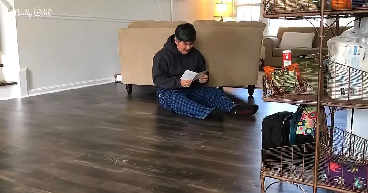 A person in pajamas sits cross-legged on a wooden floor, reading a book in a cozy living room.
