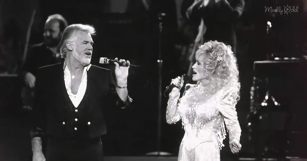 Dolly Parton and a male singer perform on stage, both holding microphones.